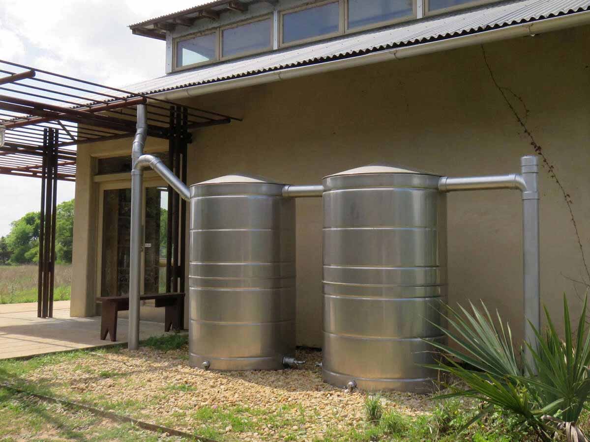 Stainless steel rainwater harvesting tanks connected by piping next to a building