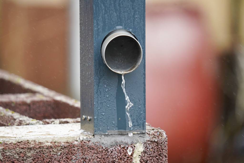 Rainwater dripping from metal downspout during rainfall